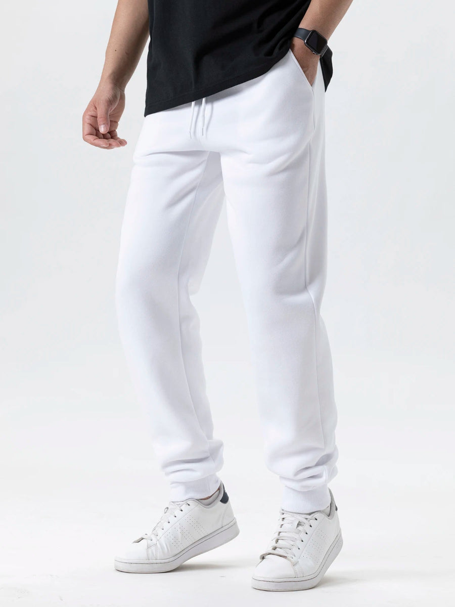 Person wearing white sweatpants and white sneakers on a plain background