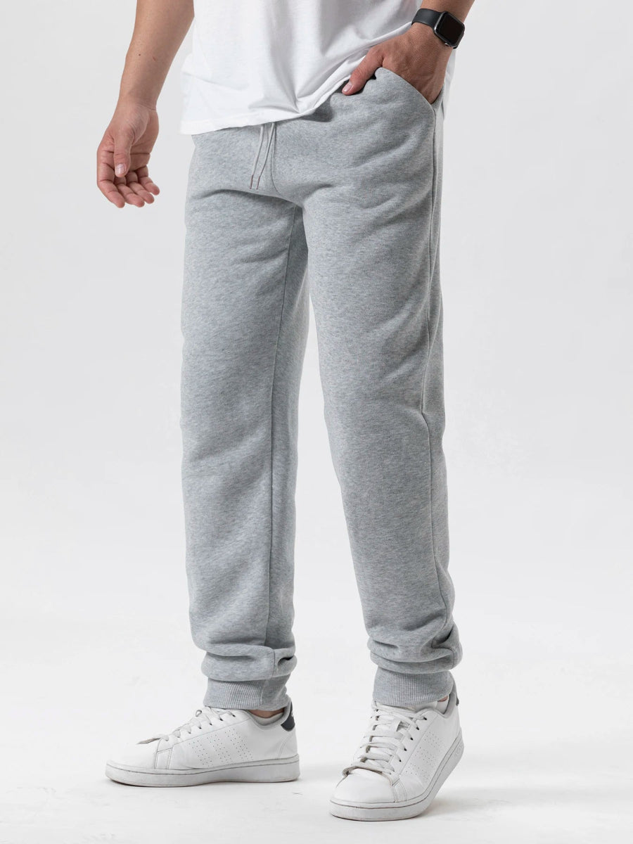 Person wearing gray sweatpants and white sneakers on a plain background